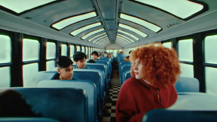 Kids on a school bus with a person with red hair and a red hoodie in the foreground